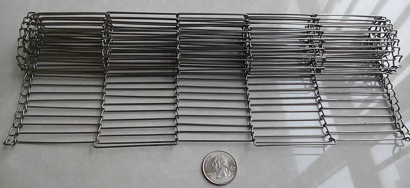 A roll of flat flex conveyor belt with part stretching out is beside a metal coin.