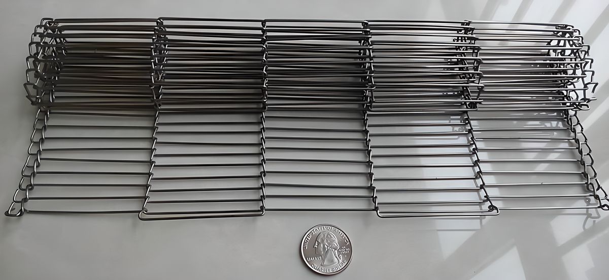A roll of rod network conveyor belt with part stretching out is beside a metal coin.