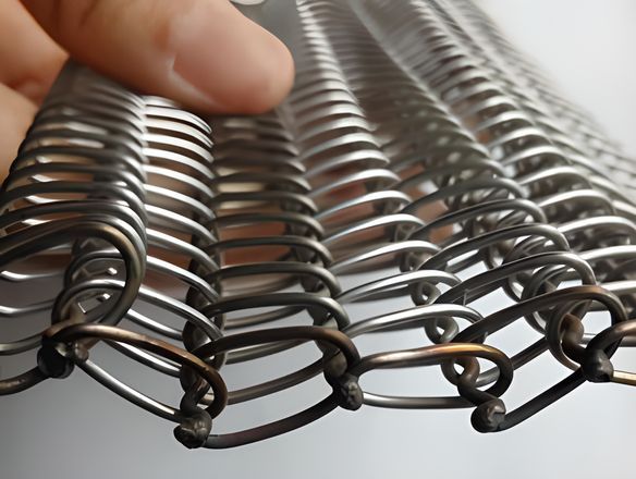A hand is holding a piece of round wire conveyor belt.
