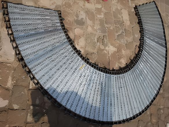 A curved perforated plate conveyor belt on the ground.