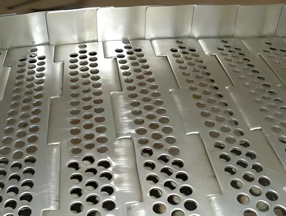 A stainless steel perforated plate conveyor belt with side guards on the ground.